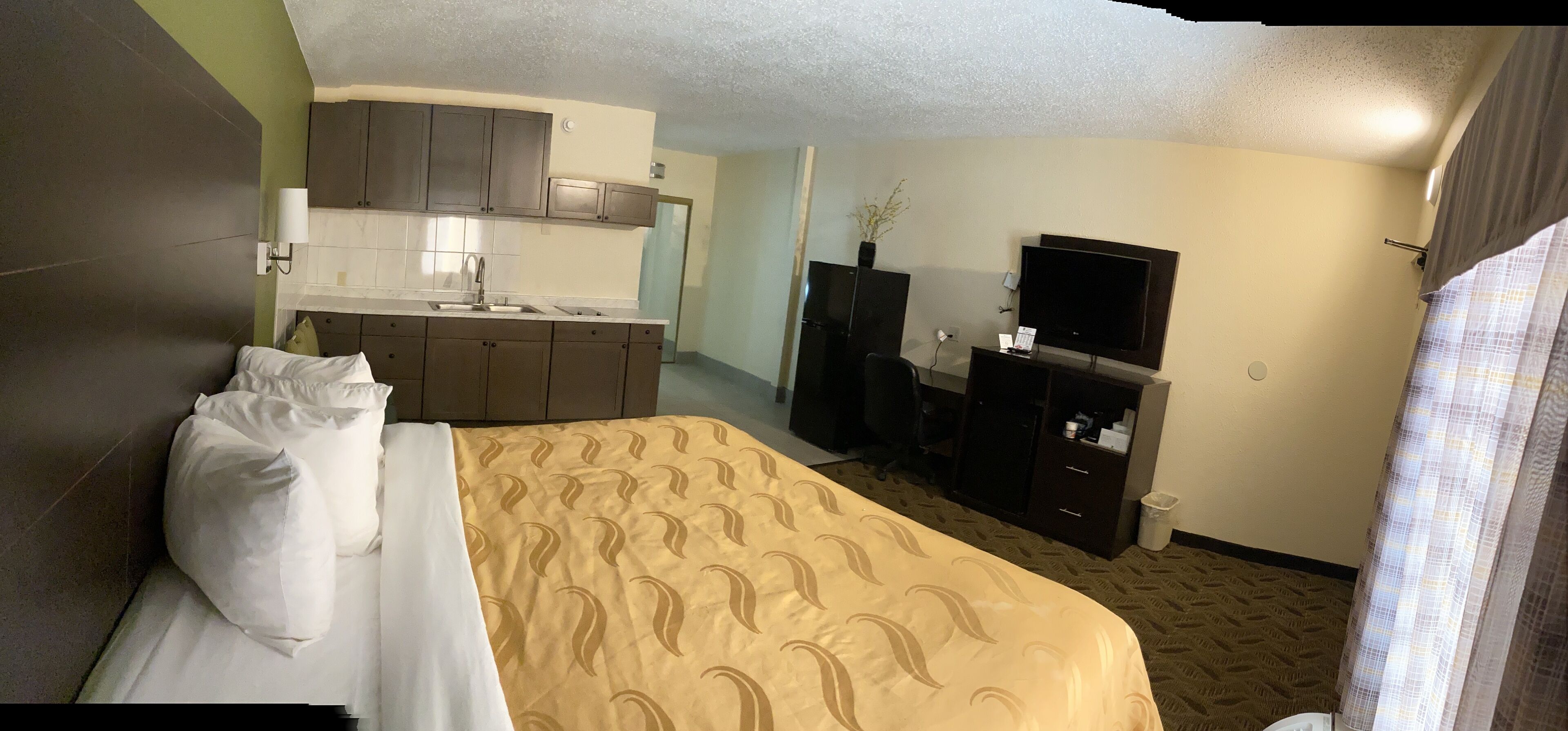 A hotel room with a bed, a desk, a television, and a kitchenette.