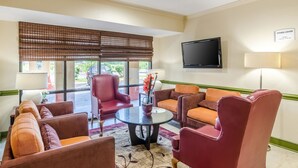 A hotel lobby with a seating area, a television, and a sign indicating the fitness center hours. - Quality Inn Tanglewood (Roanoke)