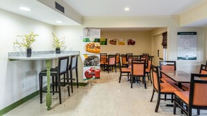 A hotel dining area with a long counter, multiple tables, and chairs. - Quality Inn Tanglewood (Roanoke)