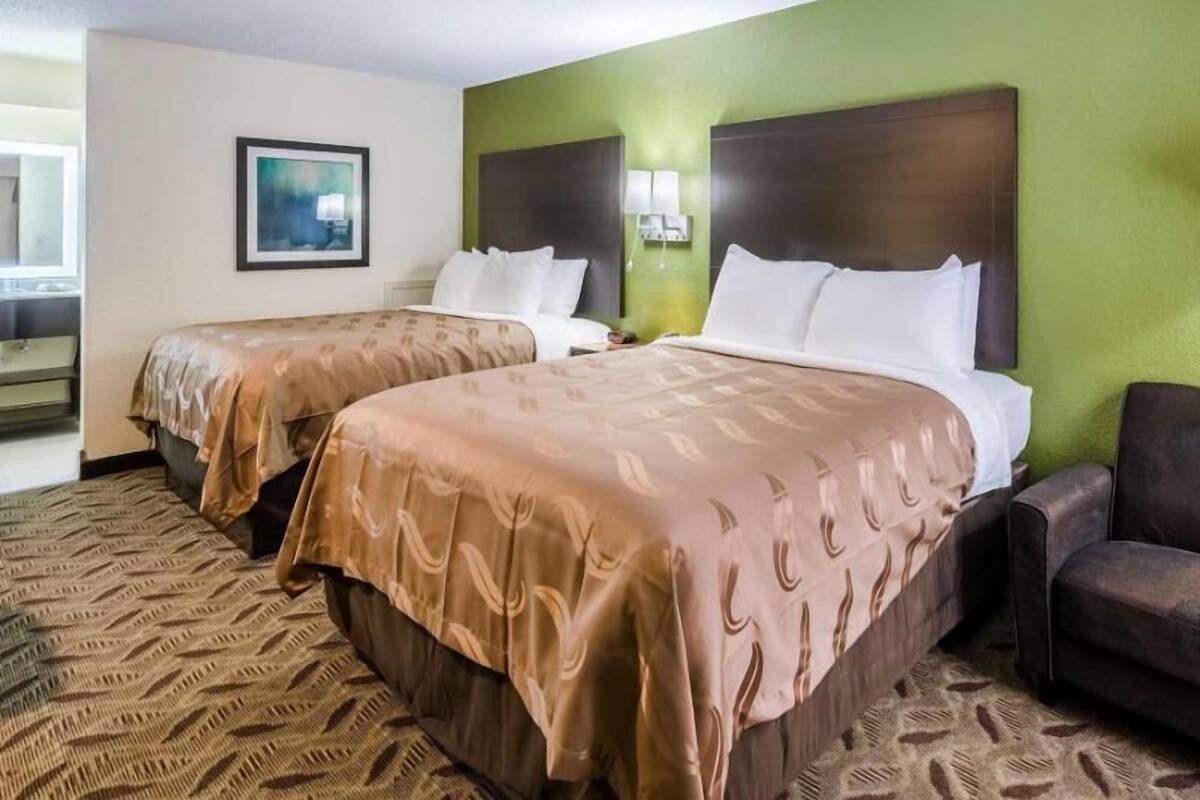 A hotel room with two beds, a green wall, a painting, and a patterned carpet.