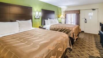 A hotel room with two beds, a green accent wall, a patterned carpet, and a door with a mirror.