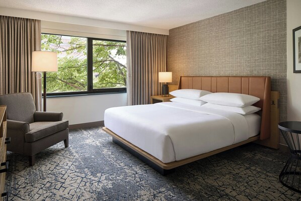 Una habitación de hotel con una cama grande, una silla, un escritorio y una ventana con cortinas.
