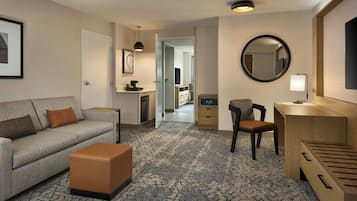Hotellihuoneessa on sohva, jalkarahi, työpöytä, tuoli ja peili. Huoneesta on ovi kylpyhuoneeseen ja käytävälle.
