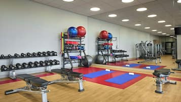 Une salle de sport équipée de bancs, d’haltères, de balles lestées et d’autres appareils d’exercice.