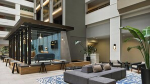 A modern lobby with a grey sectional sofa, a blue patterned rug, and a seating area with tables and chairs. - Sheraton Suites Chicago O'Hare (Rosemont)