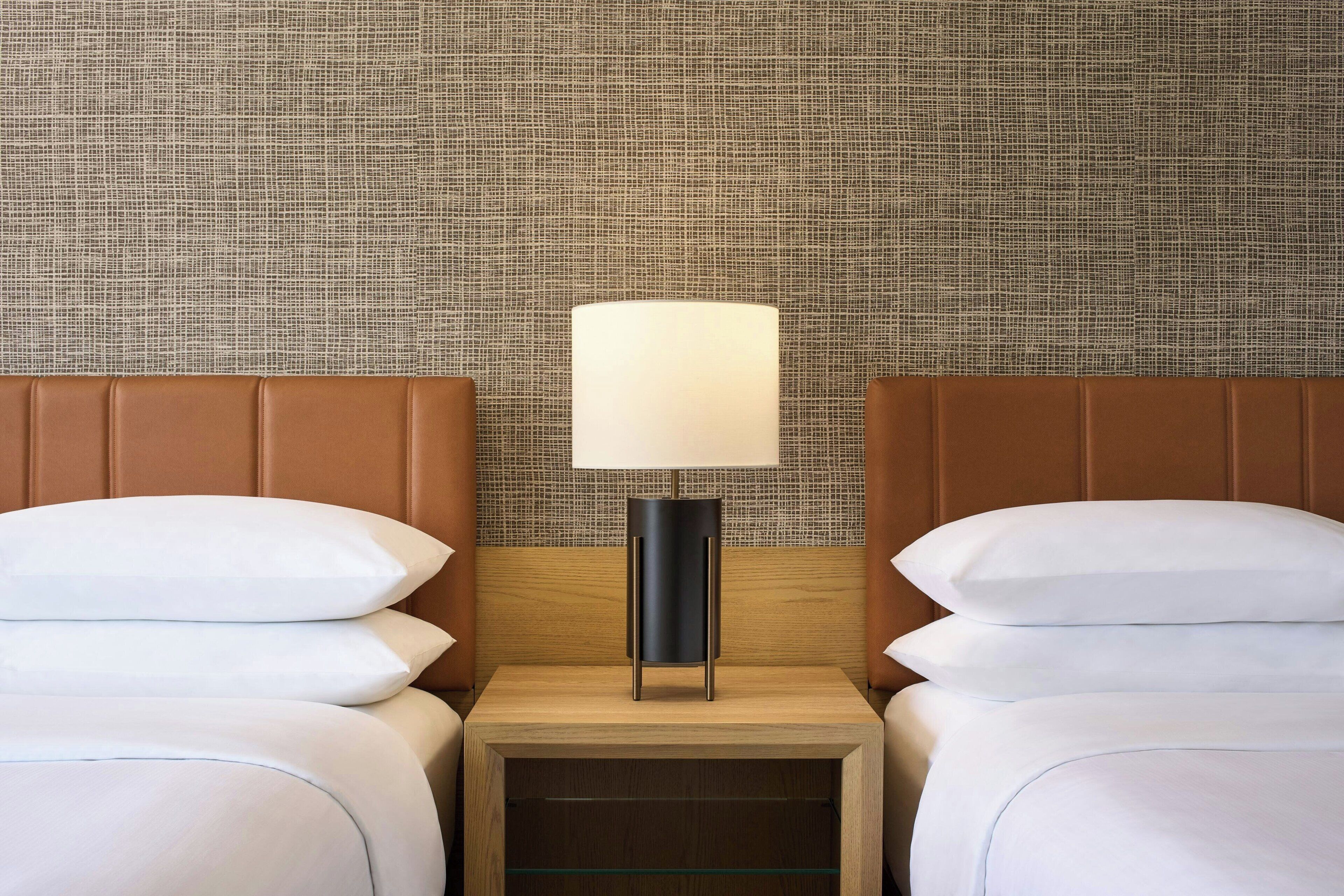A hotel room with two beds, a nightstand, and a lamp.