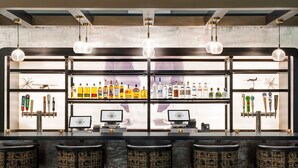 A bar with multiple shelves of liquor bottles, a cash register, and bar stools. - Sheraton Suites Chicago O'Hare (Rosemont)