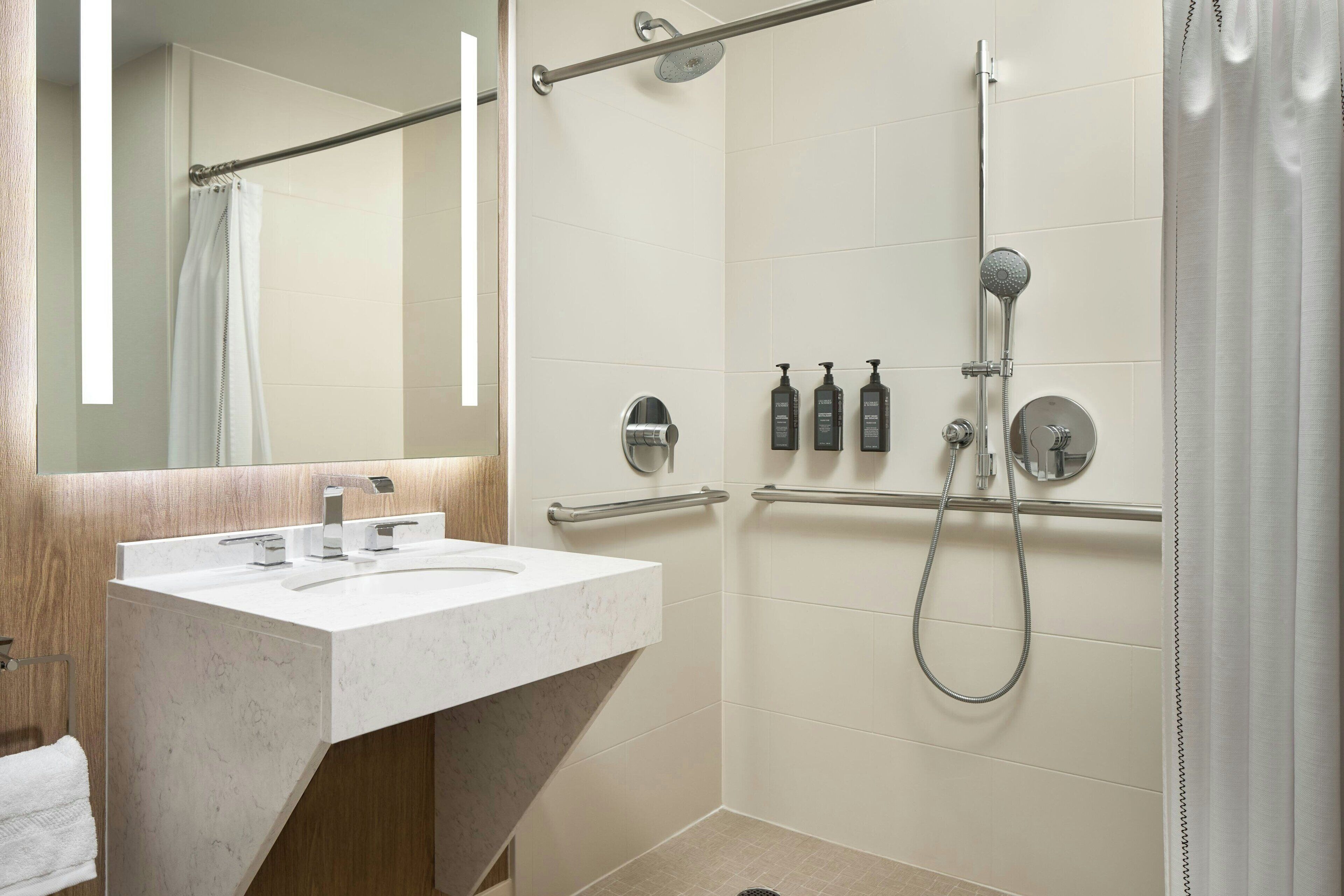 A modern bathroom with a marble sink, a shower with a handheld showerhead, and a handrail.