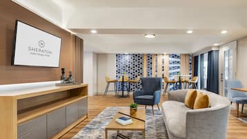 A modern hotel lobby with a reception desk, seating area, and a large screen displaying the hotel name.