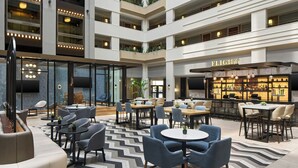 A modern hotel lobby with multiple seating areas, a bar, and a staircase connecting the floors. - Sheraton Suites Chicago O'Hare (Rosemont)
