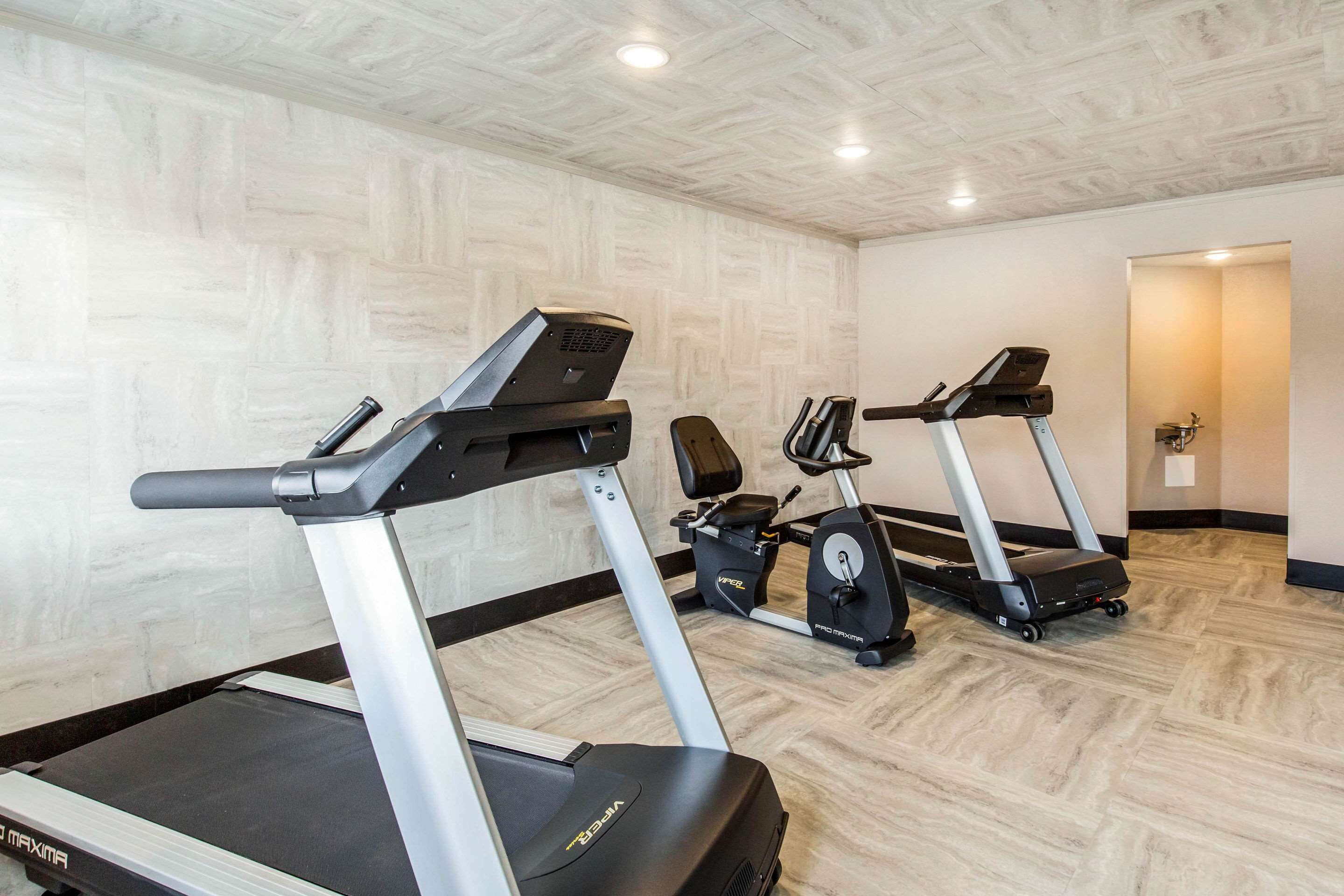 Un gimnasio con cintas de correr y bicicletas estáticas, suelo de madera y un diseño moderno en el techo.