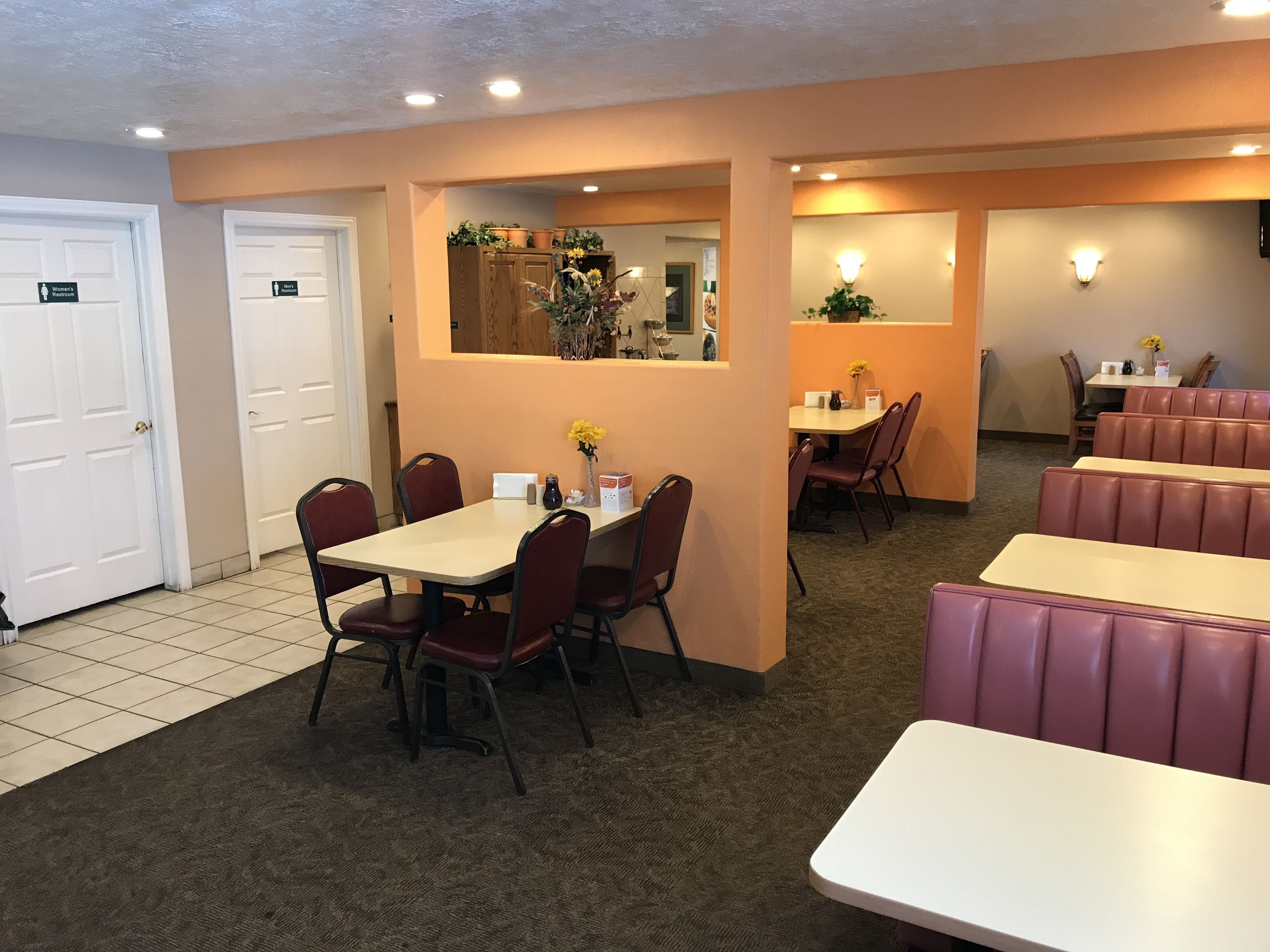 Un restaurant avec des banquettes et des tables, un espace cuisine et des toilettes pour femmes.