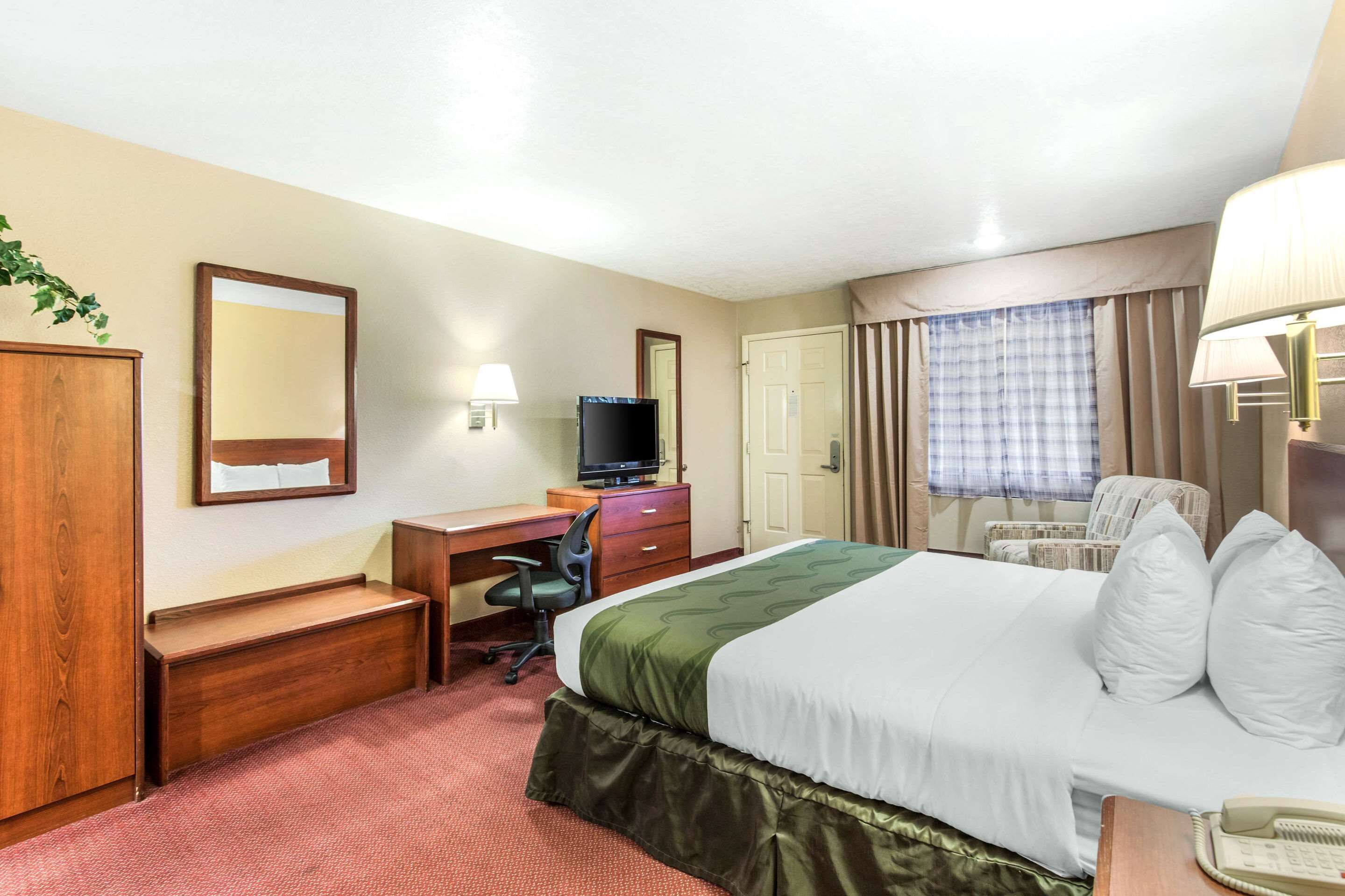 Una habitación de hotel con cama, escritorio, silla, televisión y teléfono.