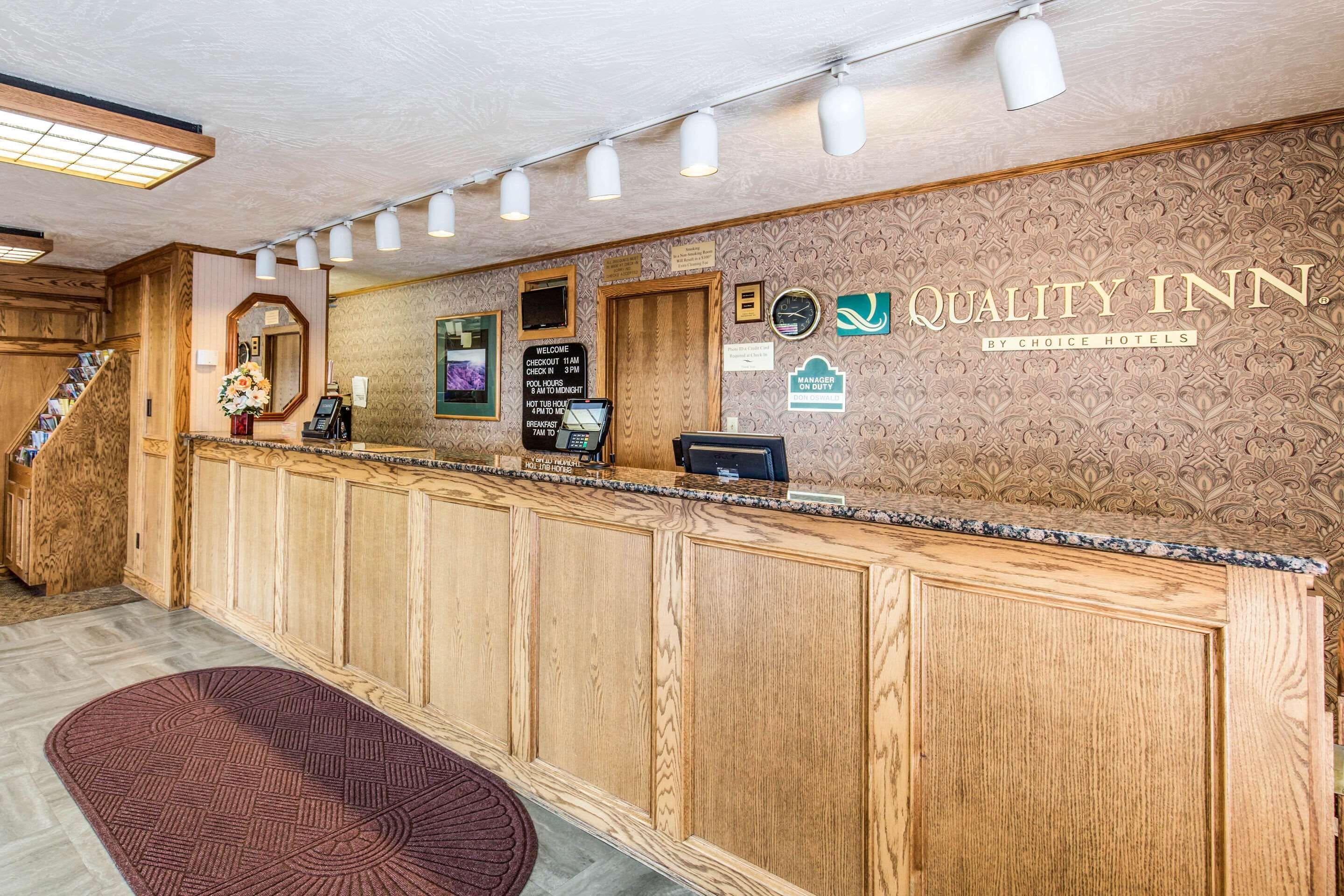 Un espace d’accueil avec un comptoir de réception en bois, une horloge et une enseigne indiquant « Quality Inn by Choice Hotels ».