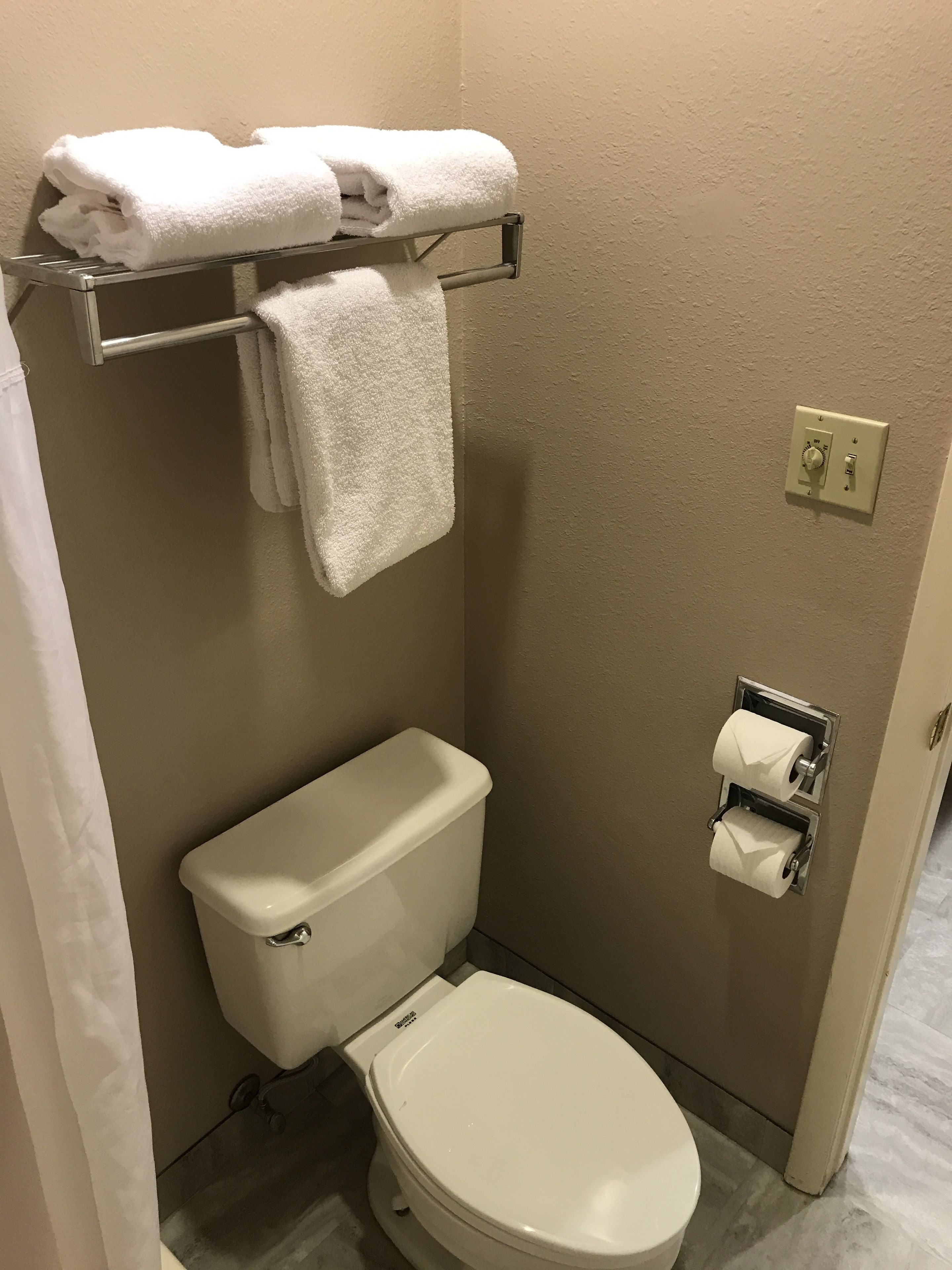 A small, clean bathroom with a white toilet, a towel rack with folded towels, and a paper towel dispenser.