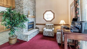 A room with a stone fireplace, a large potted plant, a wooden desk with a computer, and a red carpet. - Quality Inn Cedar City - University Area (Cedar City)