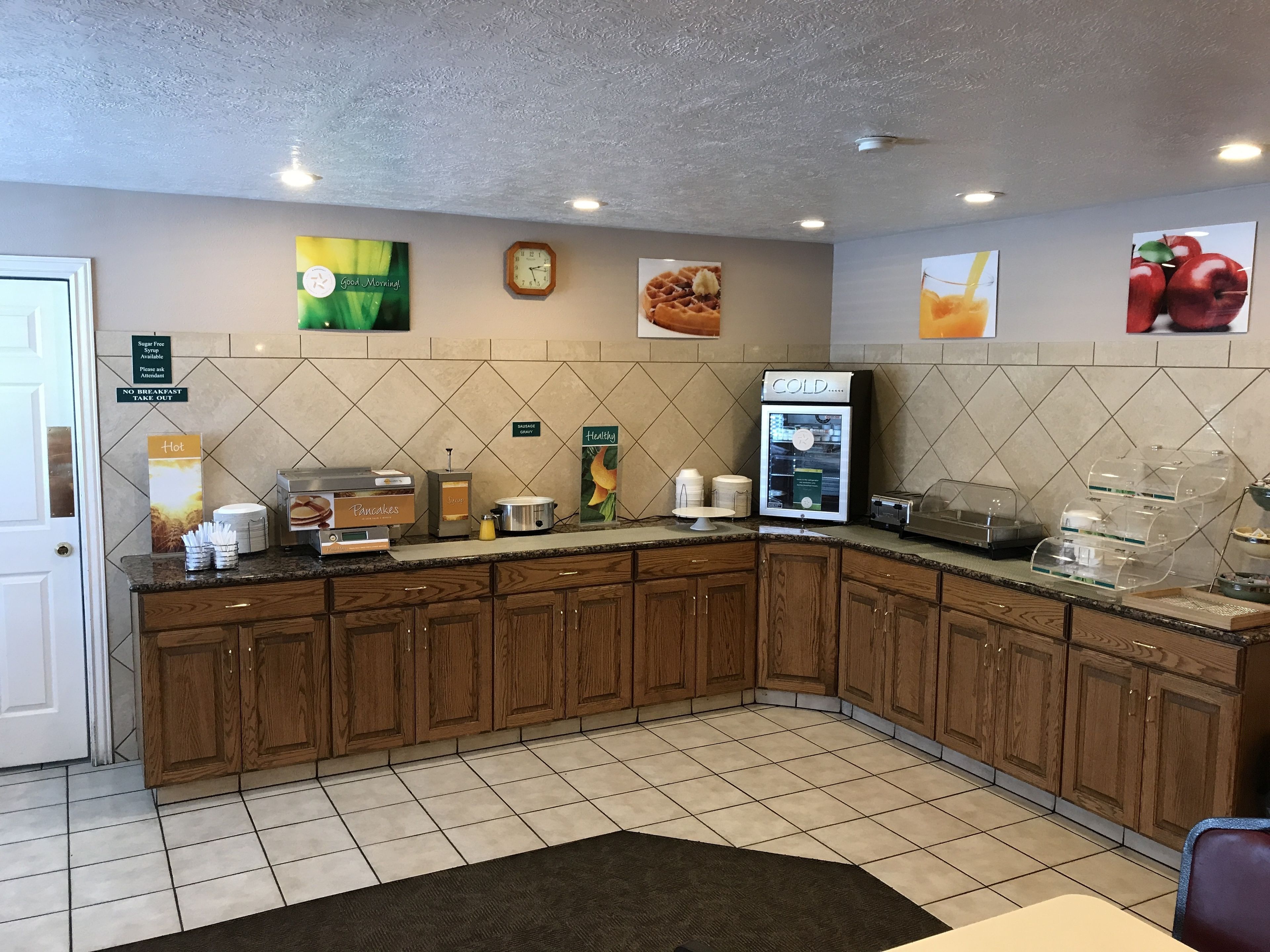 A hotel kitchen with a breakfast bar, a coffee machine, and various food items displayed on the wall.