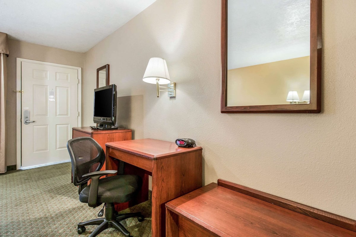 A hotel room with a wooden desk, a chair, a television, a lamp, and a mirror.