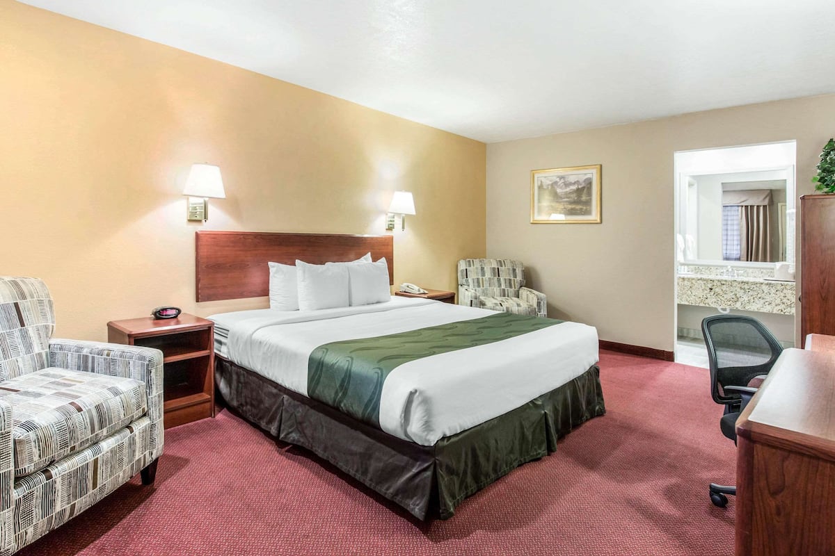 A hotel room with a large bed, two bedside lamps, a chair, a desk, and a small nightstand.