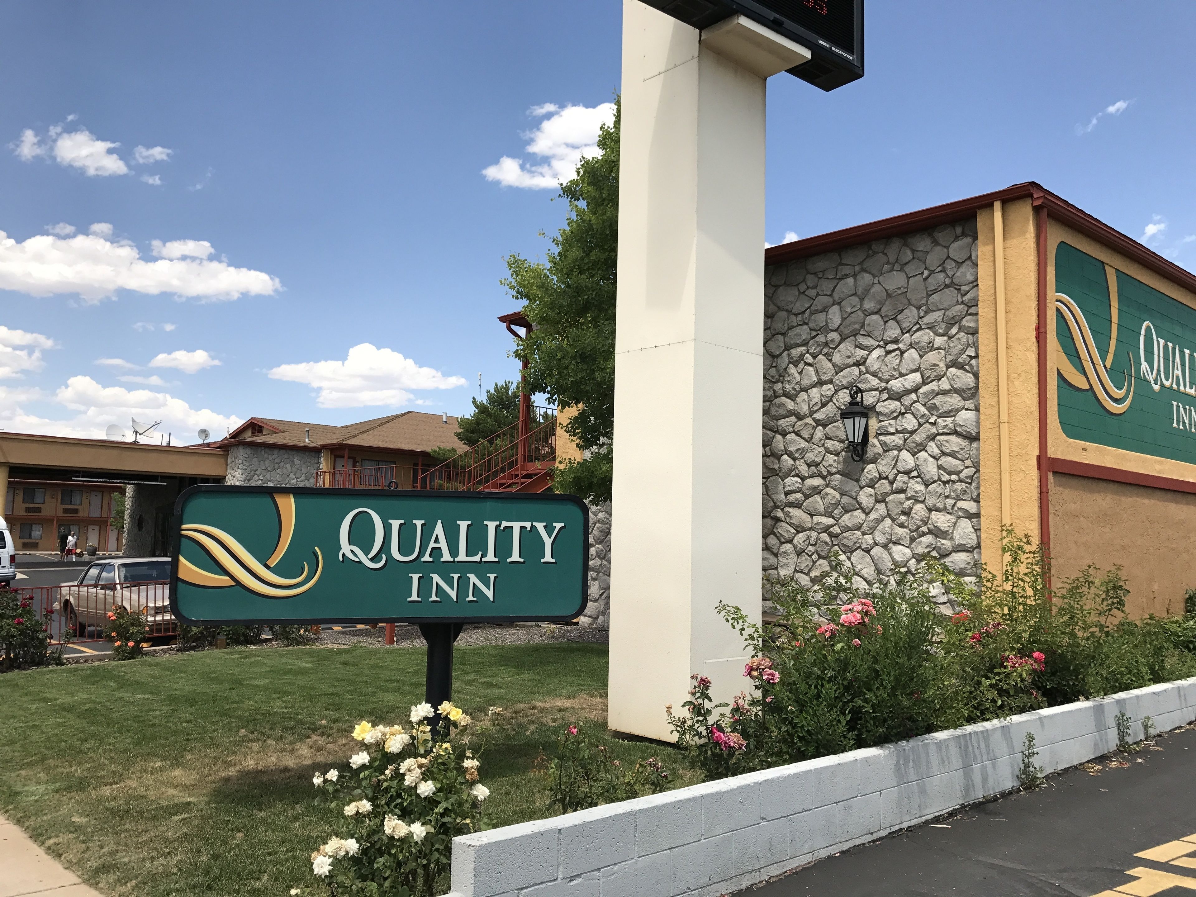 A Quality Inn sign with a stone facade and a clear sky.