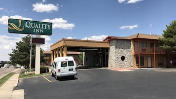 Un hôtel Quality Inn, reconnaissable à son enseigne bien visible, avec un fourgon garé devant et un bâtiment doté d’une façade en pierre et d’un balcon.