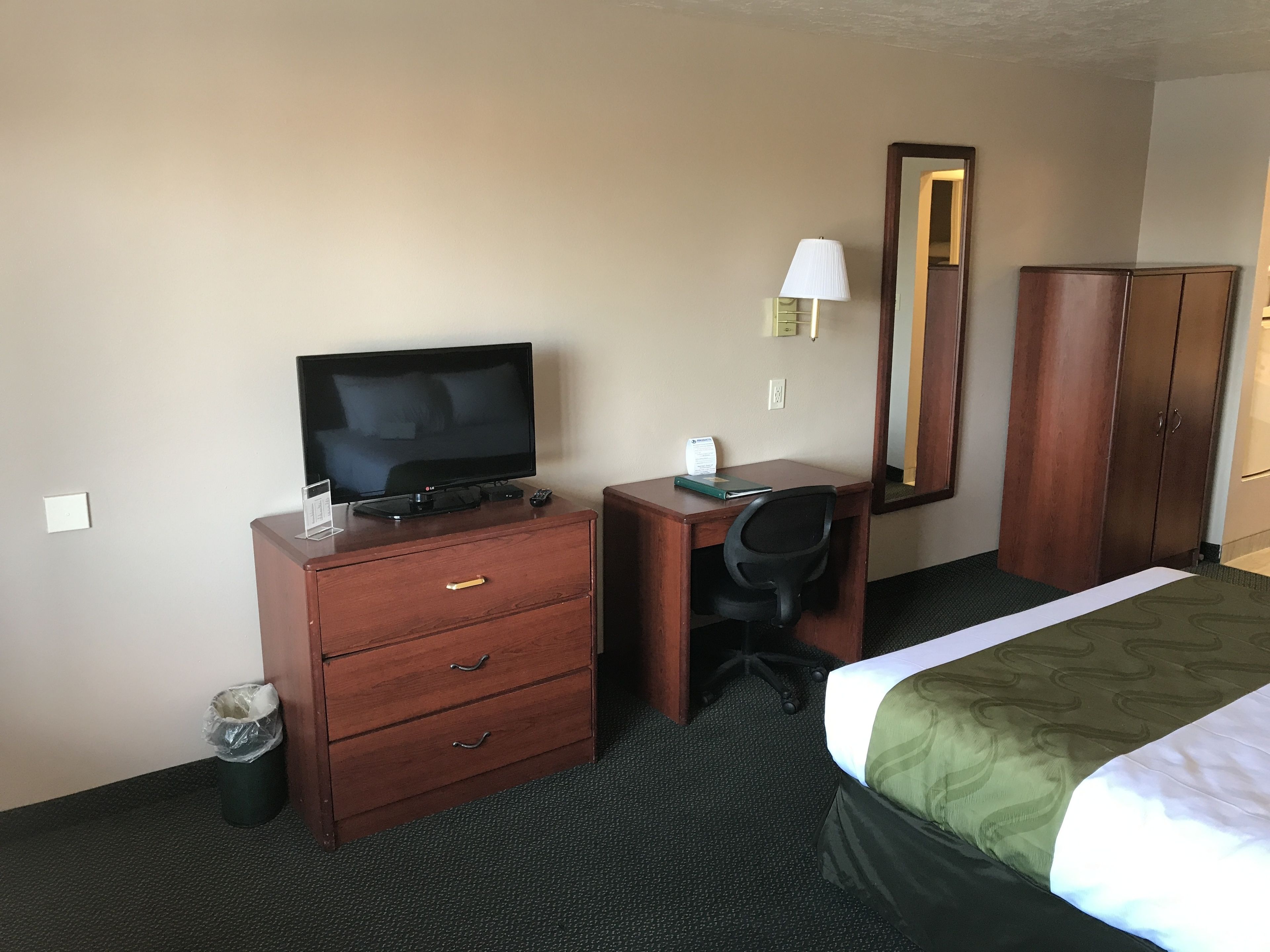 Habitación de hotel con cama, escritorio, silla, televisor, armario y un cesto de basura.