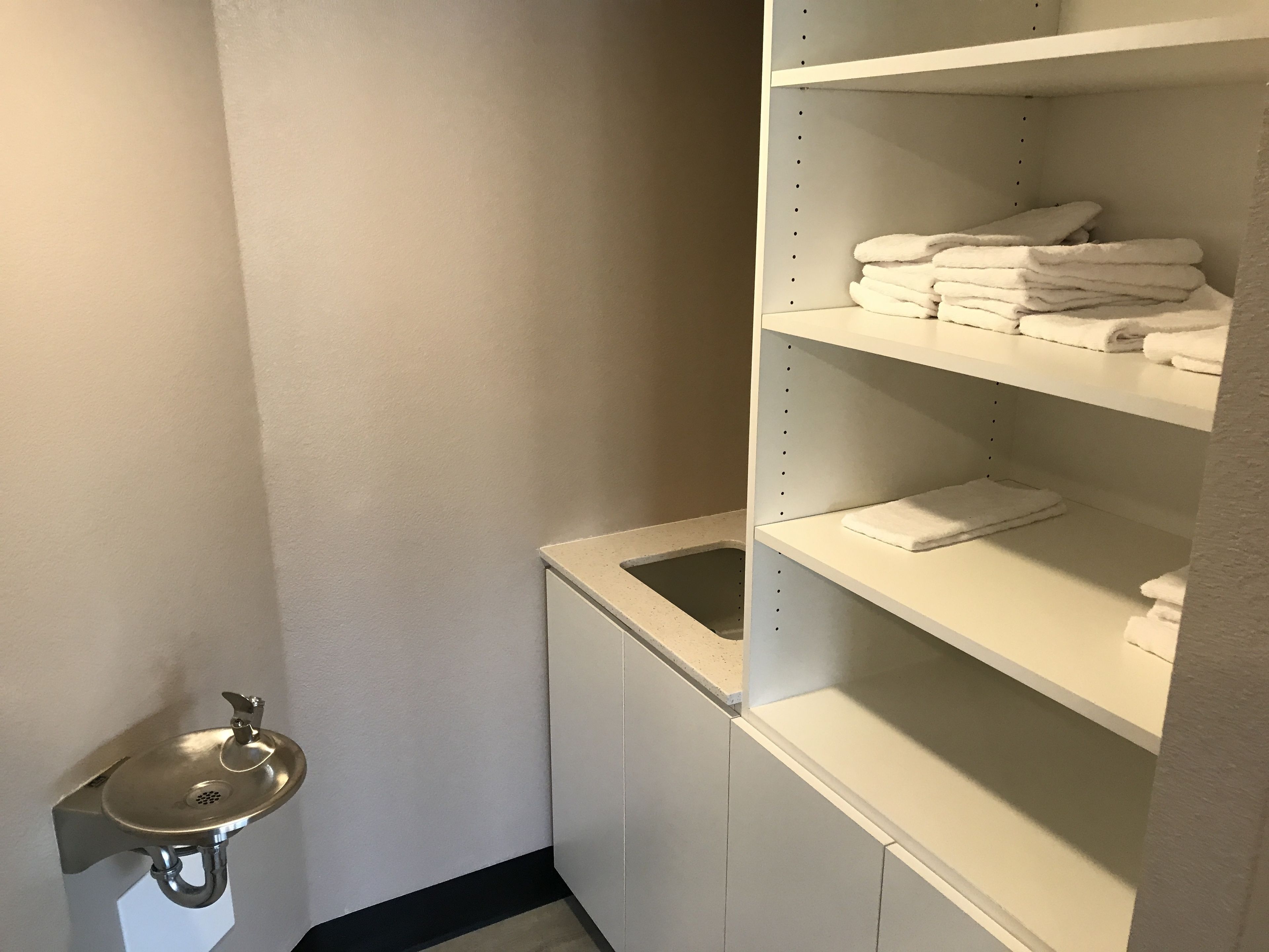 Ein Badezimmer mit Waschbecken, Spiegel und Regalen mit gefalteten Handtüchern.