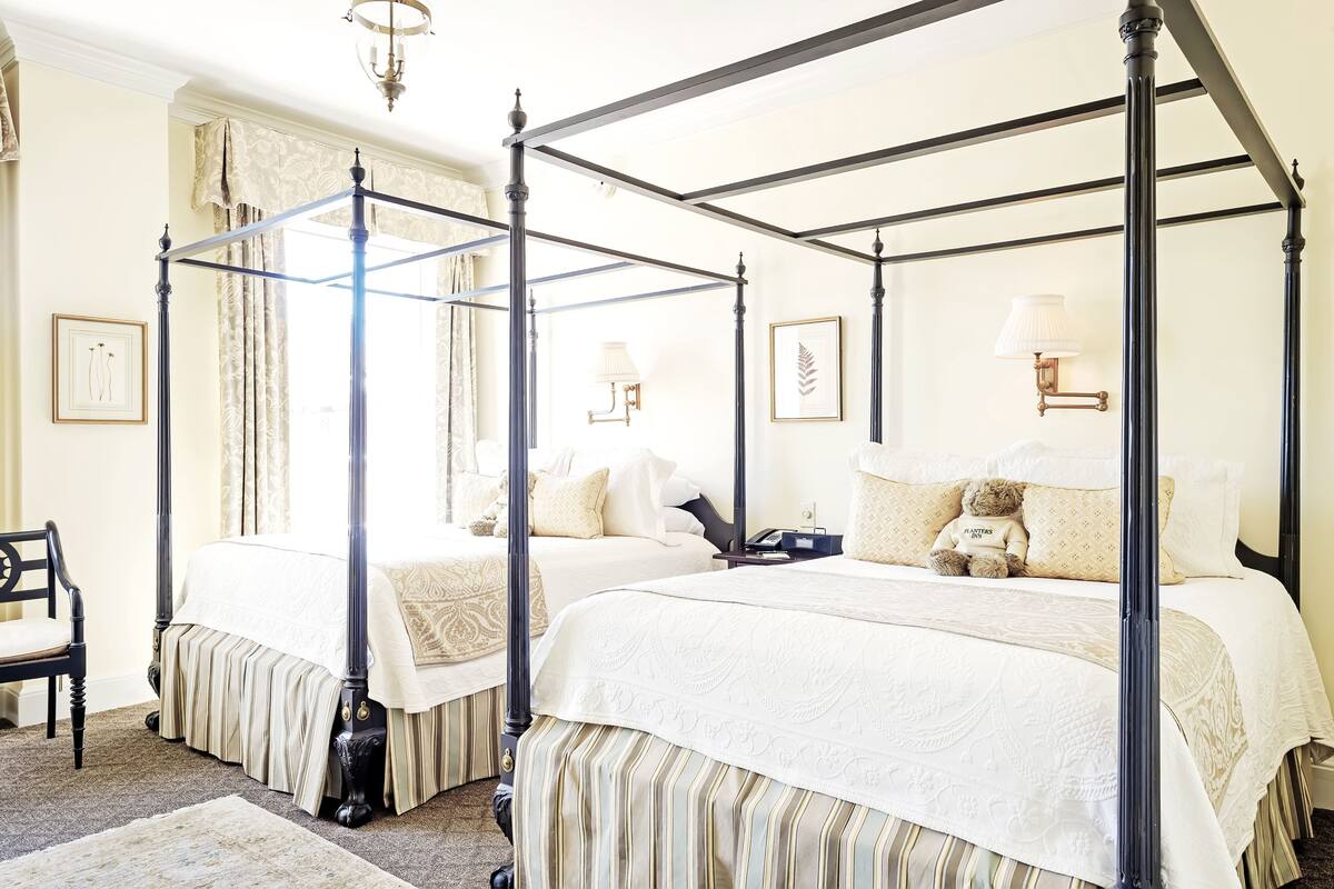 A four-poster bed with a teddy bear, a chair, and a lamp on the bedside table.