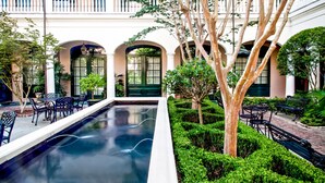 Un patio con piscina, bancos y un edificio con ventanas y balcones de arco.