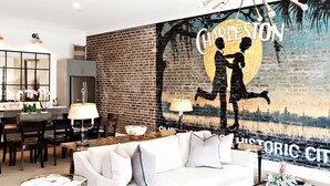 A modern living room with a white sofa, a glass coffee table, and a mural of Charleston.