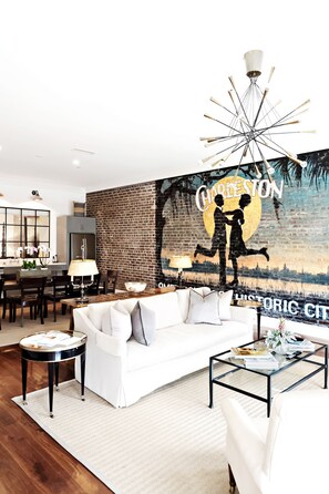 A modern living room with a white sofa, a glass coffee table, and a mural of Charleston.