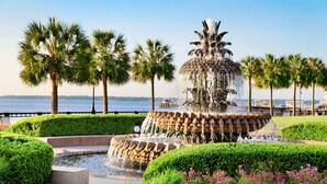 A fountain with water cascading down multiple tiers, surrounded by well-manicured hedges and palm trees.