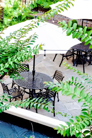 An outdoor patio with round tables and chairs, surrounded by greenery.