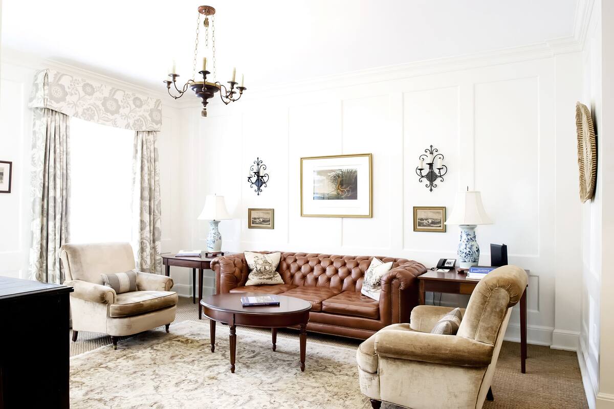 A living room with a brown leather sofa, beige armchairs, a coffee table, and a chandelier.