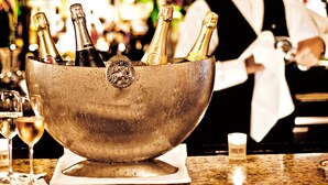 Una zona de bar con un bol de madera que contiene varias botellas de champán, copas y una vela sobre una encimera.
