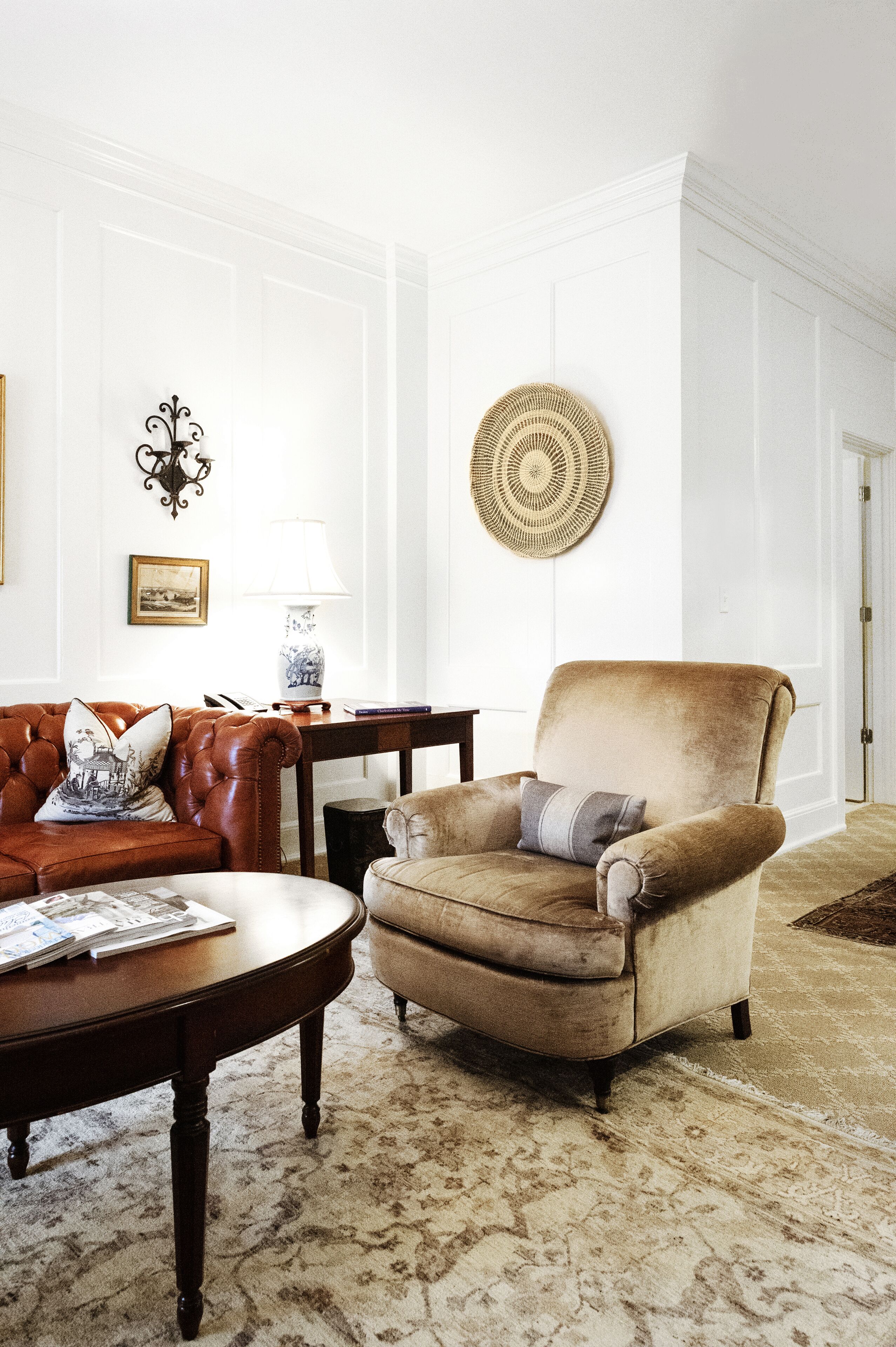 Una sala de estar con un sofá de cuero marrón, un sillón beige, una mesa de centro de madera y una alfombra estampada.