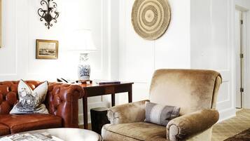 Una sala de estar con un sofá de cuero marrón, un sillón beige, una mesa de centro de madera y una alfombra estampada.