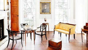 A room with a wooden floor, a sofa, a table, chairs, and a fireplace.