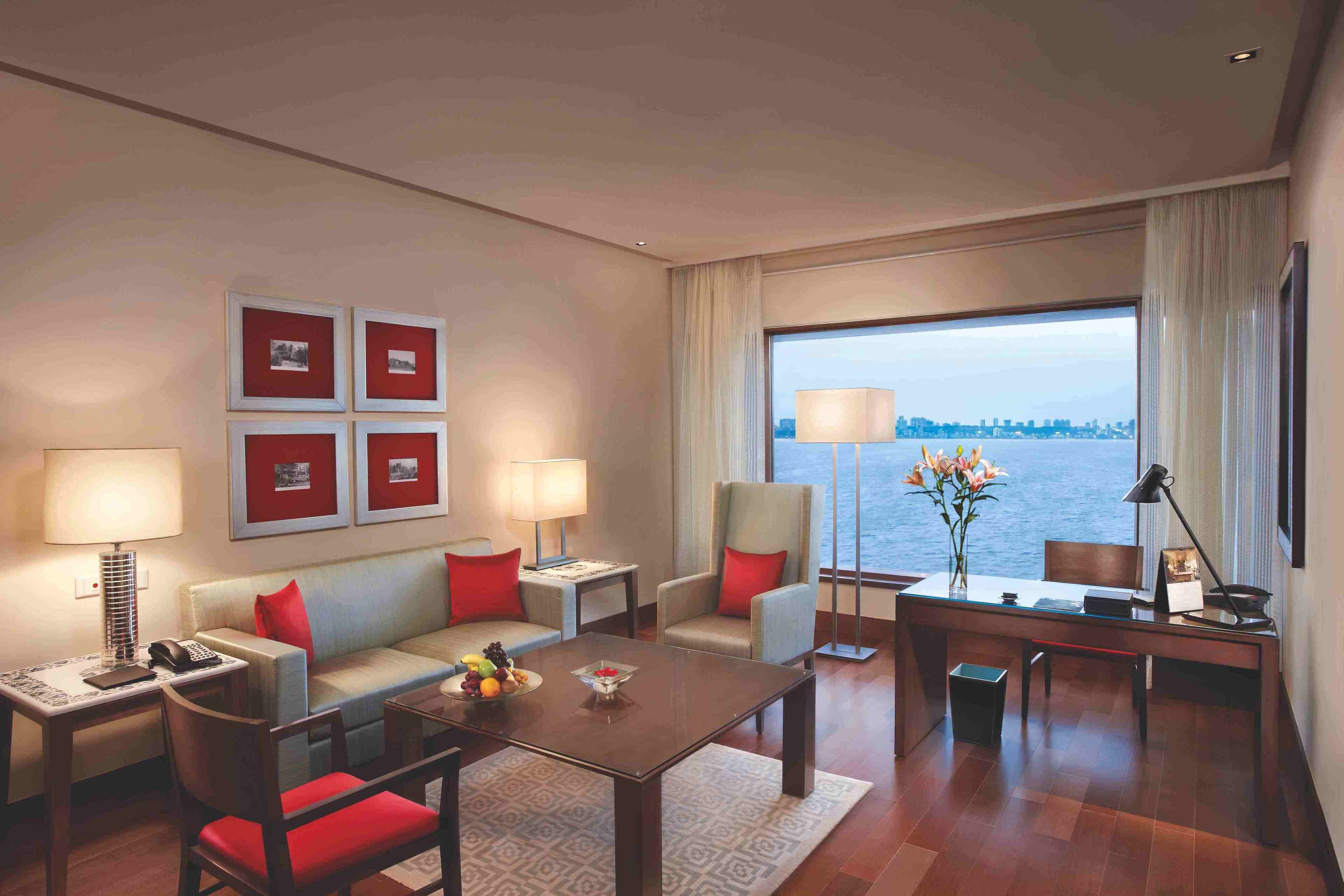 A hotel room with a sofa, armchairs, a desk, and a view of the water.