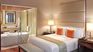 Quarto de hotel com uma cama grande, banheiro separado com banheira, um banco e mesa de cabeceira com abajur.