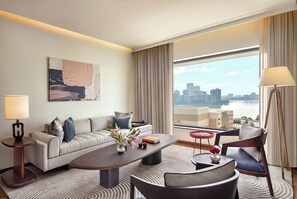A modern hotel room with a sofa, coffee table, and chairs, a large window with a city view, and a painting on the wall. - The Oberoi Mumbai (Mumbai)