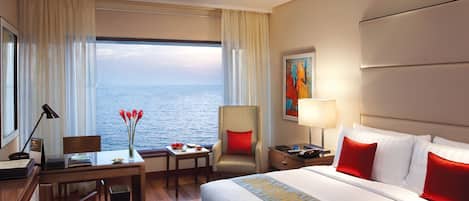 A hotel room with a bed, desk, chair, and a view of the sea.