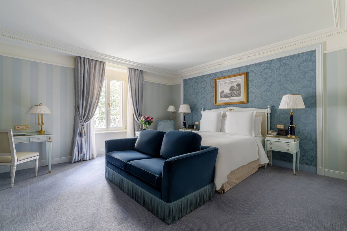 Une chambre d’hôtel avec un lit, un canapé bleu, un bureau et une table de chevet.