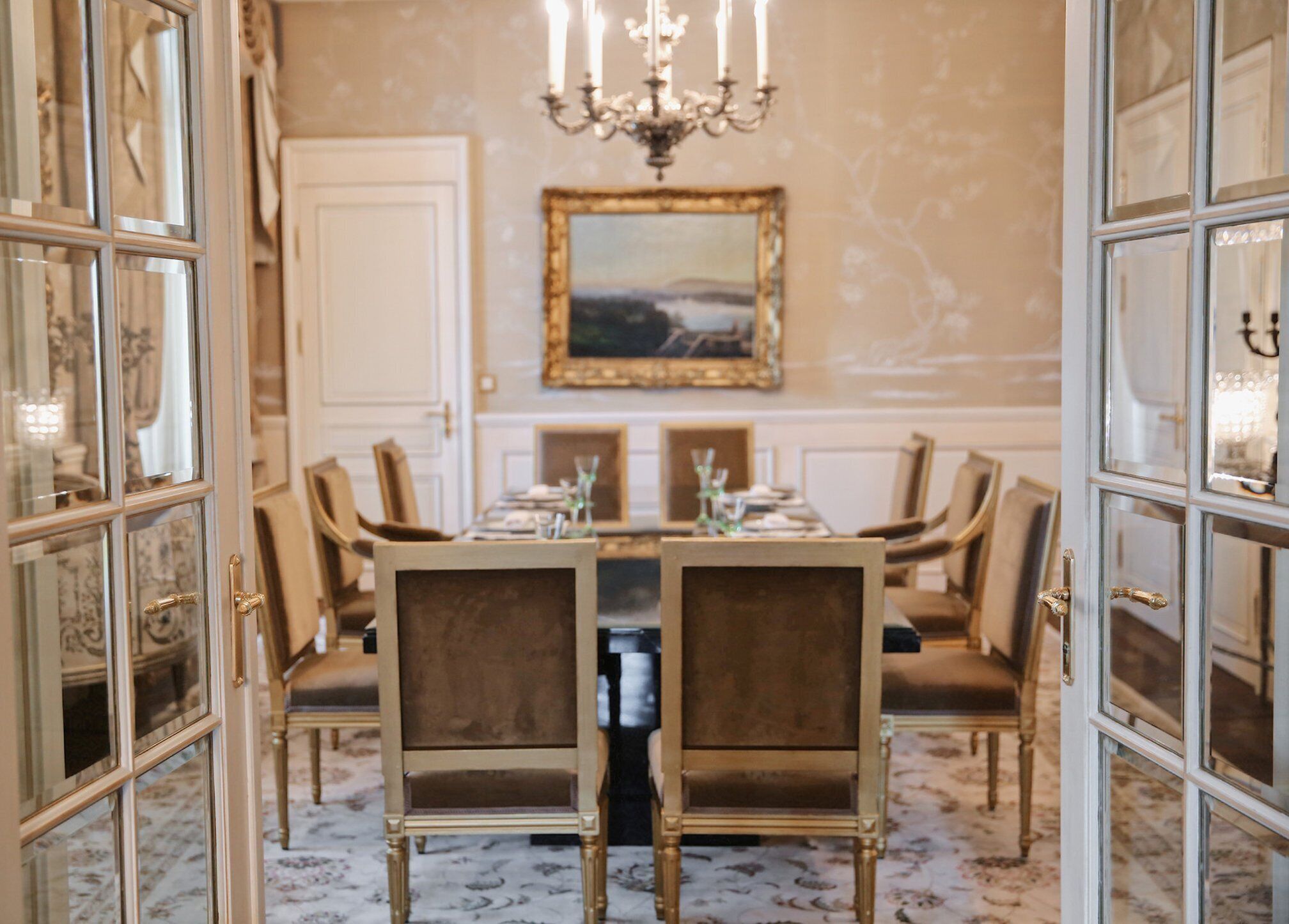 Un comedor formal con una araña, un cuadro enmarcado en la pared y una mesa lista para seis personas.