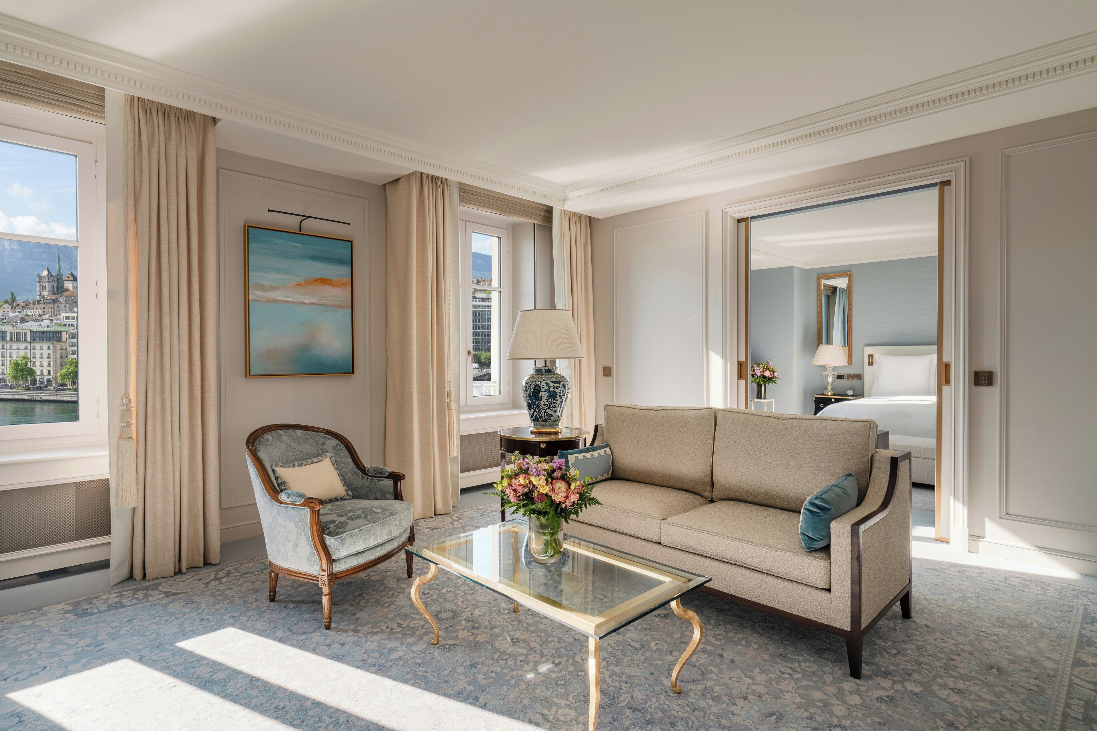 Ein Hotelzimmer mit einer Couch, einem Sessel und einem Glastisch mit Blumen.