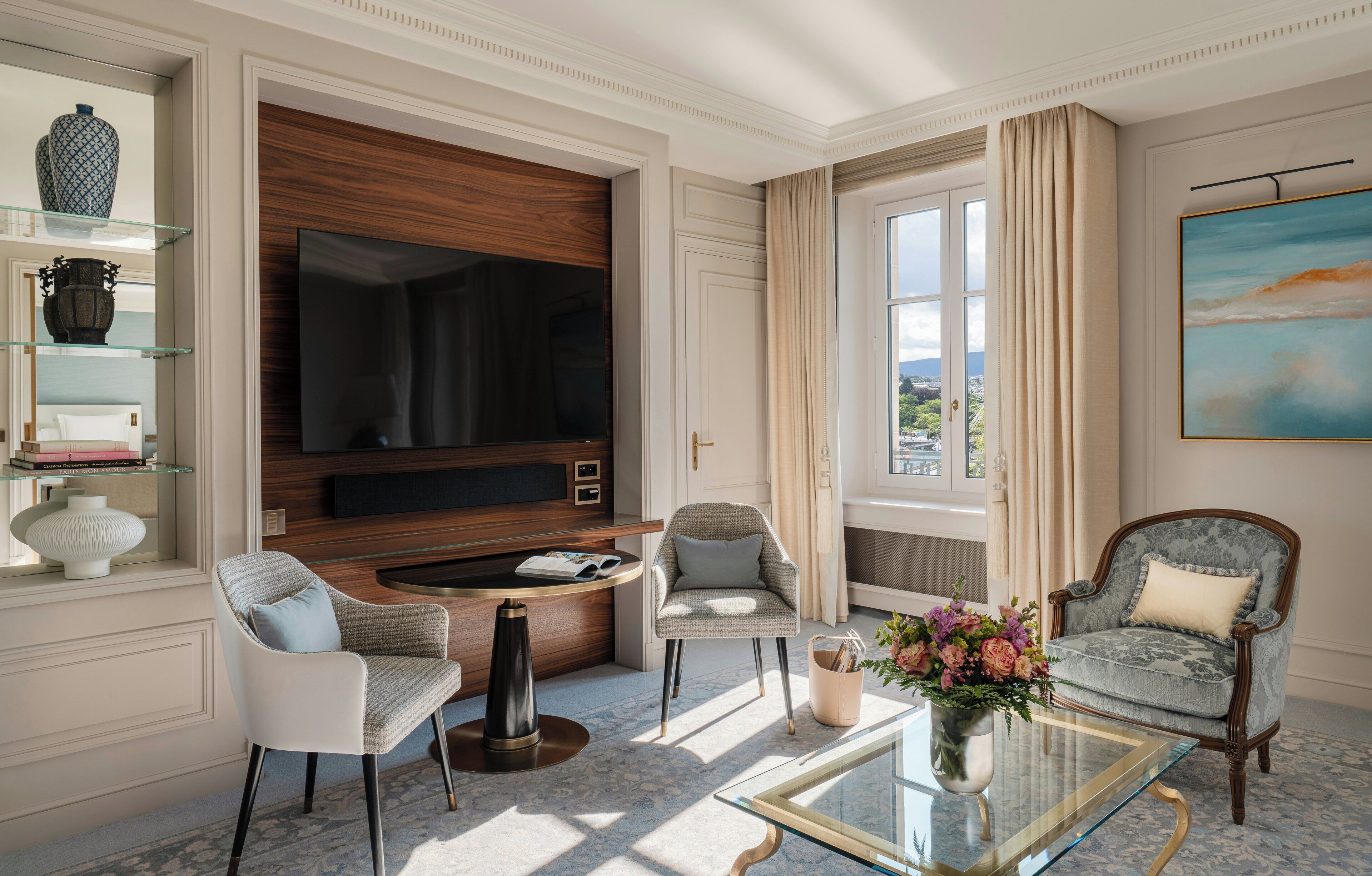 Un salon bien éclairé, doté d’un grand téléviseur à écran plat, de deux fauteuils, d’une table basse et d’une bibliothèque.