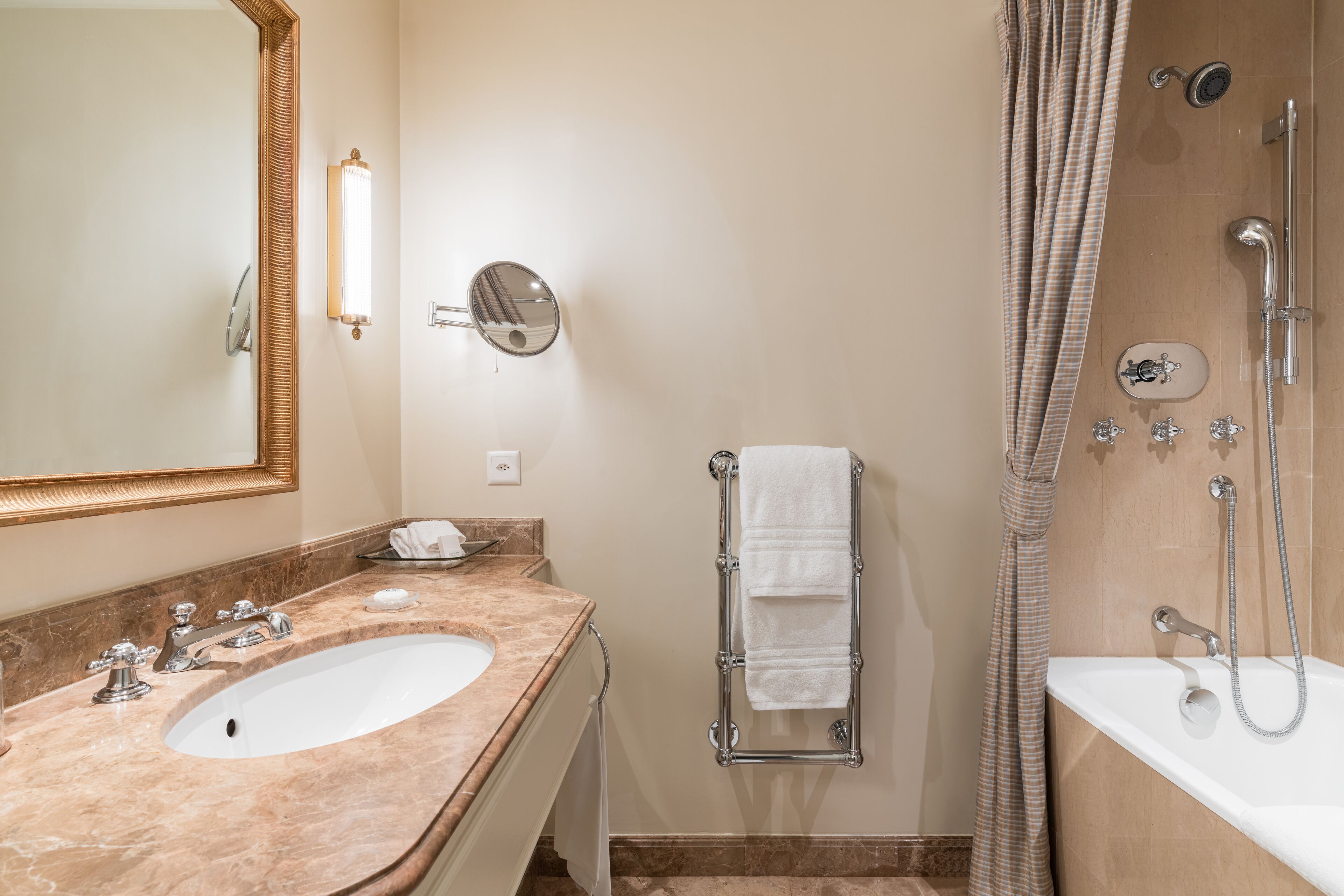 A bathroom with a marble sink, a large mirror, a towel rack, a shower with a handheld showerhead, and a bathtub.