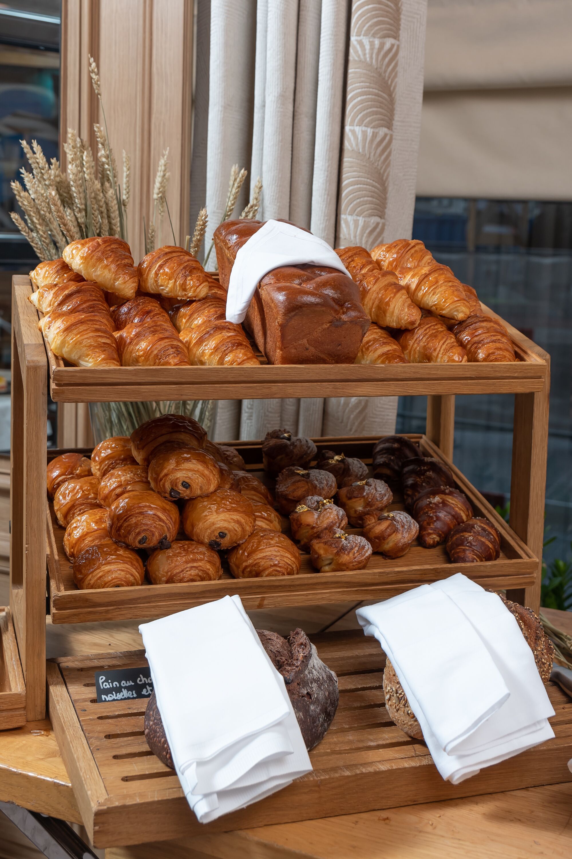 A wooden display of assorted pastries and bread, including croissants and baguettes, with a sign indicating a selection of chocolate and nutella items.