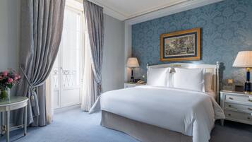 A bedroom with a large bed, two bedside tables, a nightstand, a framed picture on the wall, and a window with curtains.