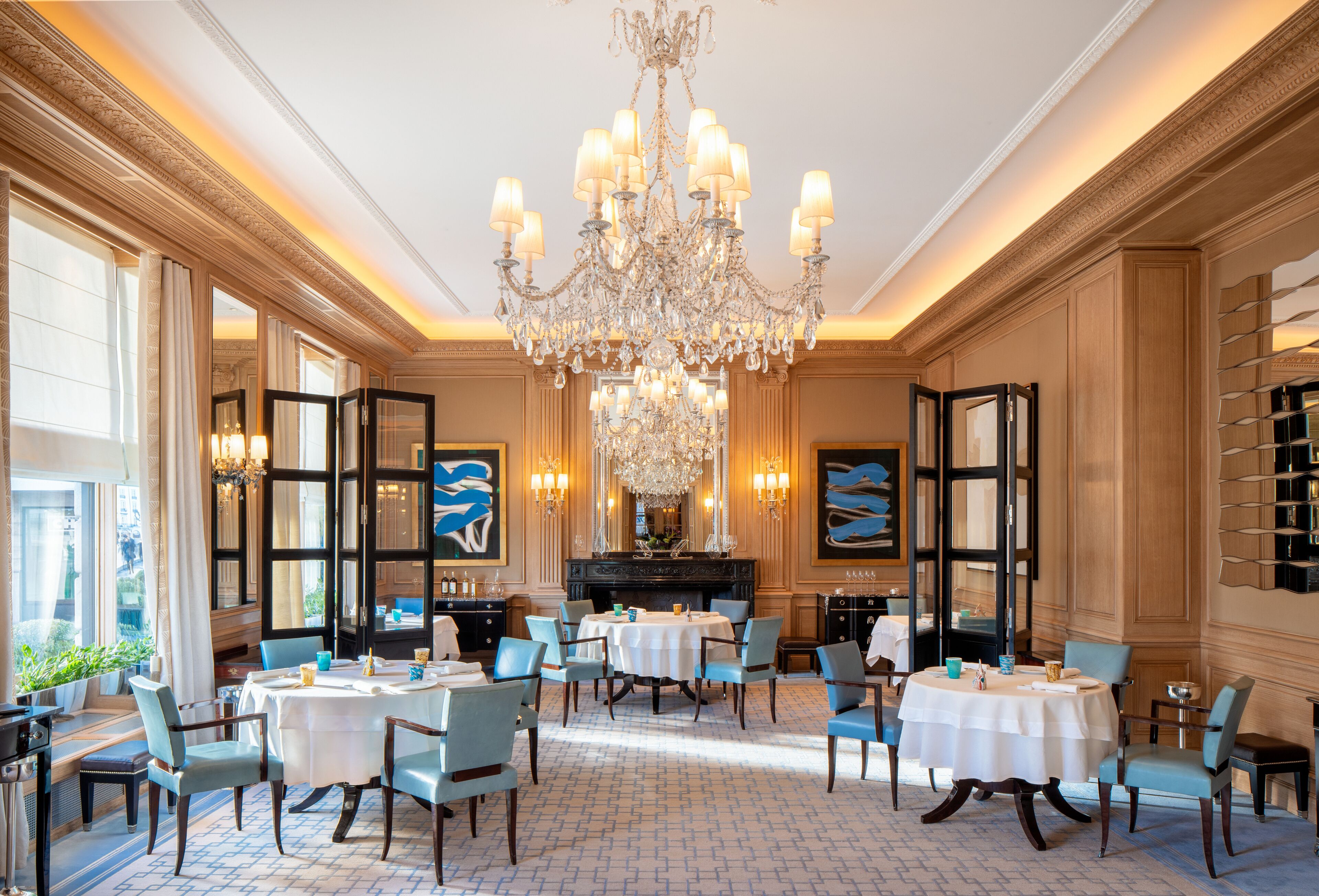 Un comedor amplio con candelabro, mesas redondas y sillas azules.